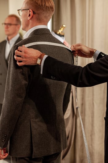 Tailor measuring the shoulder width on a man with brown made to measure blazer